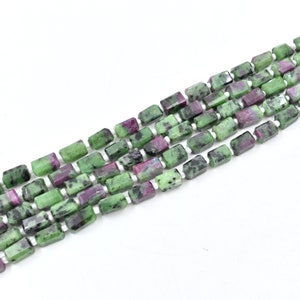 May include: Strands of rectangular beads in shades of green and magenta. The beads are strung together on white string, creating a textured and colorful pattern. The beads are likely made of natural stone, and are suitable for jewelry making.