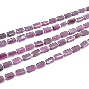 May include: A strand of pink ruby gemstone beads, each bead is rectangular and faceted. The beads are strung on a white thread.