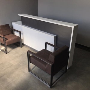 May include: Two brown leather chairs with black metal frames sit in front of a white and dark gray reception desk.