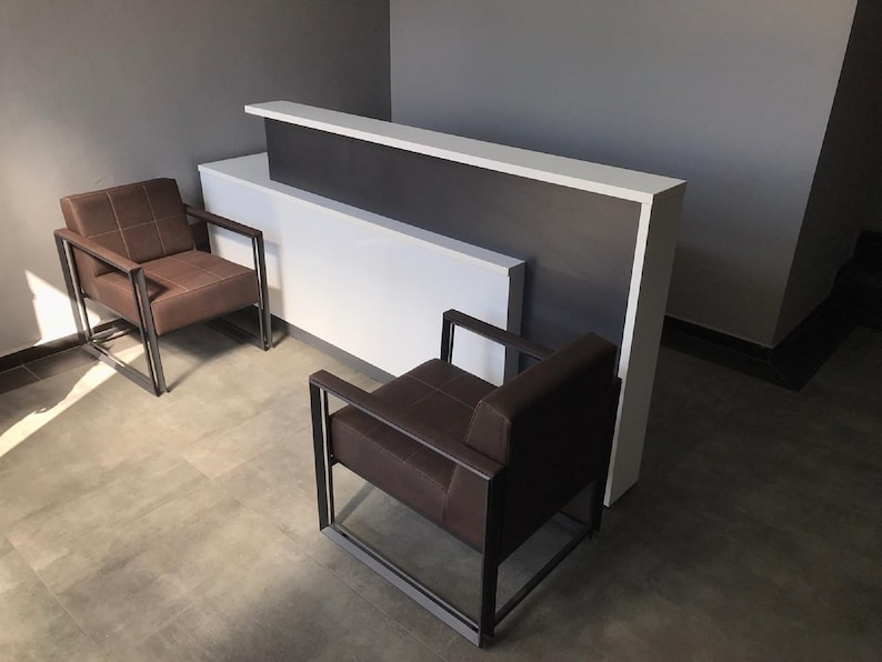 May include: Two brown leather chairs with black metal frames sit in front of a white and dark gray reception desk.