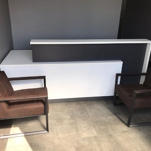 May include: A white reception desk with a dark gray countertop and two brown leather chairs with black metal frames.