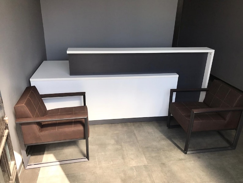 May include: A white reception desk with a dark gray countertop and two brown leather chairs with black metal frames.