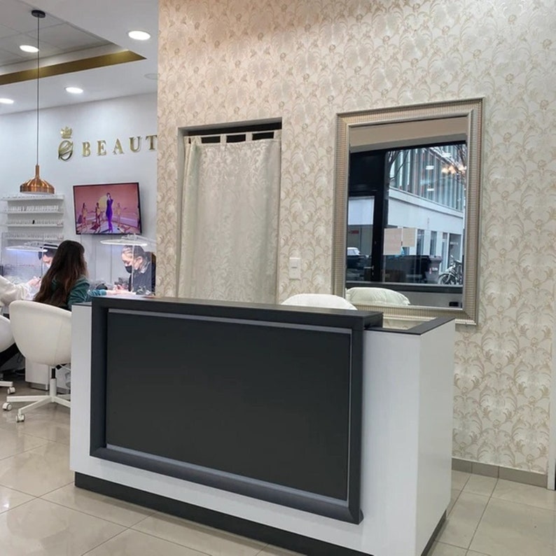 Puede incluir: Un mostrador de recepci&oacute;n blanco y negro con una pantalla negra en un sal&oacute;n de belleza. El sal&oacute;n tiene un techo blanco con molduras doradas y una pared con estampado blanco y dorado.