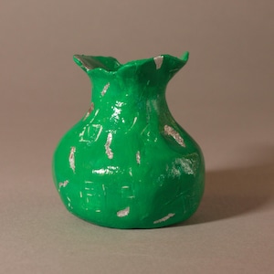 Könnte beinhalten: Eine kleine, handgefertigte grüne Vase mit gerüschtem Rand. Die Vase hat einen abgerundeten Körper und ist mit einer glänzenden grünen Oberfläche bemalt. Silberne Akzente sind am Rand und am Körper sichtbar und verleihen einen Hauch von Kontrast. Die Vase ist ein dekorativer Gegenstand.