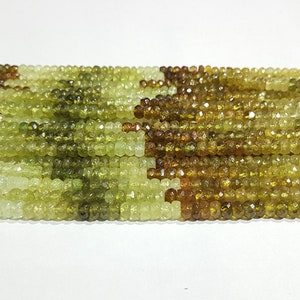Pode incluir: Um fio de contas de pedras preciosas facetadas verdes e marrons. As contas são pequenas e redondas, e são enfiadas em um fio transparente.