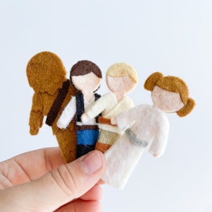 May include: Felt finger puppets of Star Wars characters. The characters include Chewbacca, Han Solo, Luke Skywalker, and Princess Leia. The puppets are brown, blue, beige, and white.