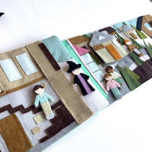May include: A felt play set with a brown house, a green house, a blue house, and a green tree. There are also four felt figures, including a witch, a boy, and two girls.