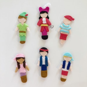May include: Six felt figures of characters from Peter Pan and the Disney movie, Peter Pan. The figures are all wearing different outfits and have different hair colors. The figures are all standing on a white background.