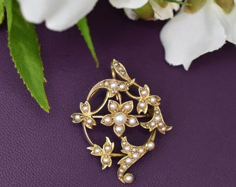 Könnte beinhalten: Goldfarbene Brosche mit floralem Design und kleinen Perlen. Die Brosche hat eine zentrale Blüte mit einer größeren Perle, umgeben von kleineren Blüten und Perlenakzenten. Der Hintergrund ist tiefviolett.