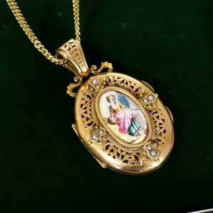 May include: A gold-toned oval locket pendant with a detailed filigree design and a small painted portrait. The locket is suspended from a gold chain. Small pearls are set around the portrait.