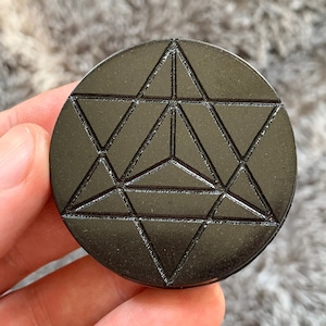May include: A black obsidian stone with a carved geometric design, resembling a star or a flower.