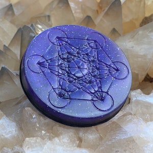 May include: A purple, glittery, round pendant with a raised, intricate geometric design. The pendant is on a bed of white crystals.