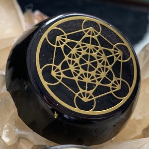 May include: Black obsidian stone with a gold geometric design, resembling a flower of life pattern.