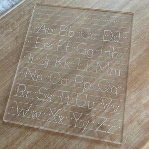 Könnte beinhalten: Ein transparentes Trockenlöschbrett aus Kunststoff mit dem Alphabet in weiß gedruckt. Die Buchstaben sind in Groß- und Kleinschreibung und alphabetisch geordnet.
