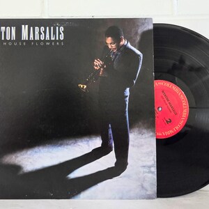 以下が含まれることがあります： Wynton MarsalisのHot House Flowersのレコードジャケットと黒いレコード盤。ジャケットには、スポットライトの下でトランペットを演奏するダークスーツ姿のミュージシャンが描かれています。レコードの中央にはColumbiaの文字が入った赤いラベルがあります。