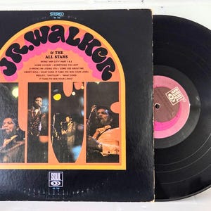 Pode incluir: Um disco de vinil preto e a sua capa quadrada de cartão do álbum Live de Jr. Walker & The All Stars. A capa tem detalhes em laranja, uma lista de faixas e três painéis fotográficos verticais com músicos a atuar no palco.