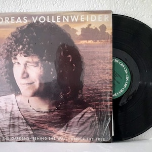 May include: A vinyl record album cover featuring a portrait of Andreas Vollenweider, a Swiss musician, with long curly hair. The album title is "Behind the Gardens - Behind the Wall - Under the Tree".