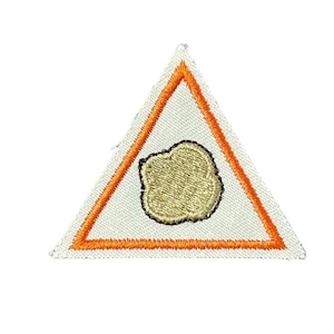 May include: Embroidered patch in the shape of a white triangle with an orange border. Inside the triangle is a gold-colored, irregularly shaped design. The patch is likely for clothing or accessories.