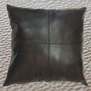May include: Black leather pillow with a stitched design. The pillow is square and has a soft, luxurious feel.