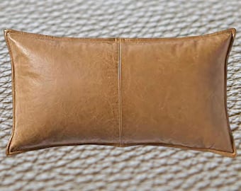 Puede incluir: Una almohada rectangular de cuero marrón con una costura en el centro. La almohada está sobre una superficie texturizada.