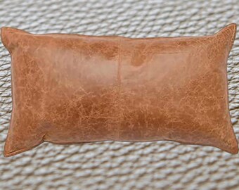 Puede incluir: Una almohada rectangular de cuero marrón con un aspecto desgastado. La almohada está hecha de cuero genuino y tiene una sensación suave y cómoda.