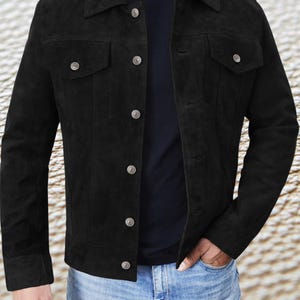 May include: A black suede jacket with a button-up front and a classic denim jacket style. The jacket has a pointed collar, two chest pockets, and two front pockets.