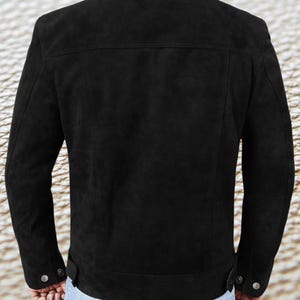 May include: A black suede jacket with a collared neckline and long sleeves. The jacket has a button closure and two pockets on the front.