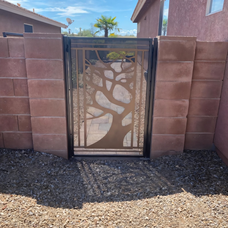 May include: A black metal gate with a tree design cut out. The tree is made of a copper-colored metal. The gate is set in a brick wall.