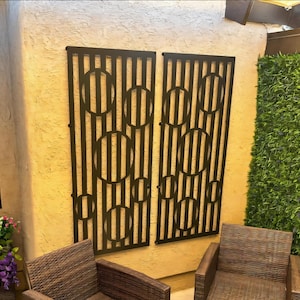 May include: Two black metal wall panels with a geometric design of overlapping circles and vertical stripes. The panels are mounted on a tan wall.