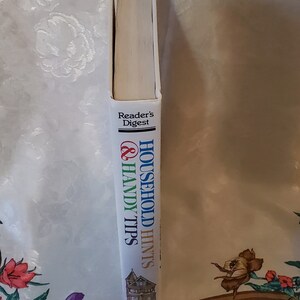 May include: A white book with blue, green, and red text that reads "Household Hints & Handy Tips" and "Reader's Digest". The book has a picture of a house on the cover.
