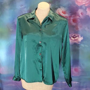 May include: A long-sleeved, emerald green satin blouse with a button-up front and a collared neckline.