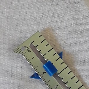 Op de afbeelding: Een zilveren liniaal met blauwe plastic markeringen, gemarkeerd in centimeters, die de nummers 1, 2, 3 en 4 tonen.
