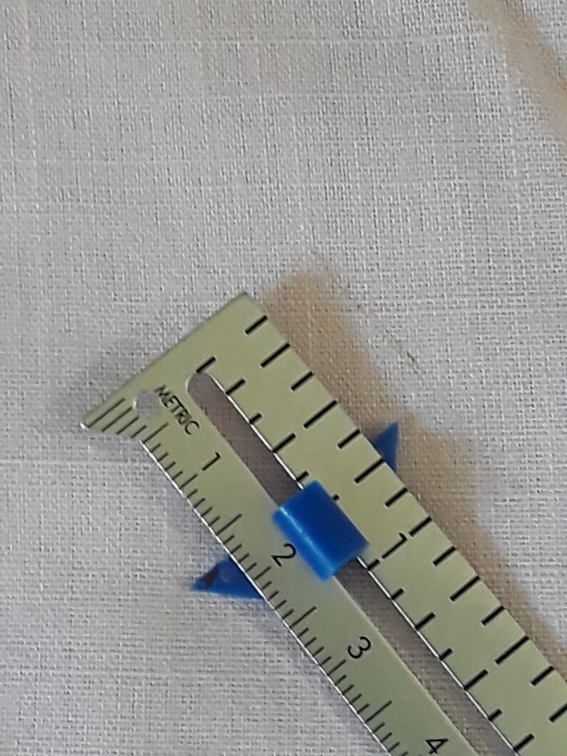 Op de afbeelding: Een zilveren liniaal met blauwe plastic markeringen, gemarkeerd in centimeters, die de nummers 1, 2, 3 en 4 tonen.
