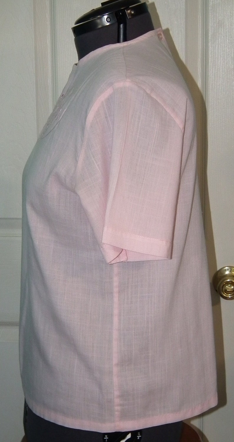 Op de afbeelding: Een lichtroze blouse met korte mouwen en een simpel ontwerp. De blouse is gemaakt van een lichtgewicht stof en heeft een licht losse pasvorm.