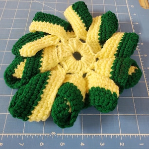 Puede incluir: Un salvamanteles de ganchillo hecho a mano con forma de flor. El salvamanteles presenta secciones alternas de hilo amarillo brillante y verde oscuro. El salvamanteles está diseñado para proteger las superficies de ollas y sartenes calientes.
