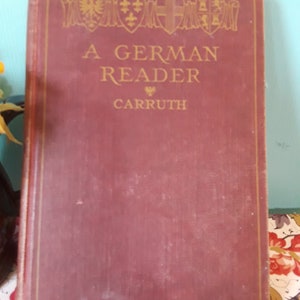 May include: A burgundy hardcover book with gold lettering on the cover. The title is "A German Reader" and the author is "Carrruth".
