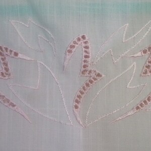 Op de afbeelding: Witte stof met roze geborduurde bloemenmotief. Het ontwerp heeft een reeks gestileerde bladeren met een zigzagpatroon.