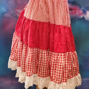 May include: A red and white gingham skirt with a white lace trim. The skirt has multiple tiers and is gathered at the waist.
