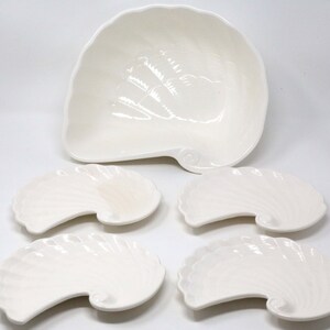 May include: A set of five white ceramic serving dishes shaped like seashells. The set includes a large, shallow bowl and four smaller, curved dishes.