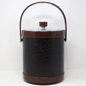 May include: A brown faux leather ice bucket with a silver lid and handle. The bucket has a textured surface.