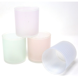 May include: Four cylindrical glass candle holders in pastel colors: purple, green, red, and blue. Each holder is decorated with small, evenly spaced dots. The holders are arranged in a group, with one tilted on its side.