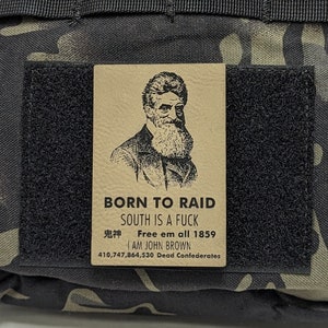 May include: A brown patch with a black and white illustration of a man with a beard. The patch has the text "BORN TO RAID", "SOUTH IS A FUCK", "Free em all 1859", "I AM JOHN BROWN", and "410,747,864,530 Dead Confederates".