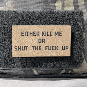 May include: A tactical bag with a camouflage pattern. A rectangular patch with the text "EITHER KILL ME OR SHUT THE FUCK UP" is attached to the bag with a velcro backing. The patch is tan with black lettering.