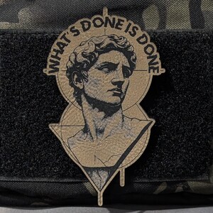May include: A tan patch featuring a classical bust within a circle and a triangle. The text "WHAT'S DONE IS DONE" surrounds the bust. The patch is affixed to a black velcro square on a camouflage background.