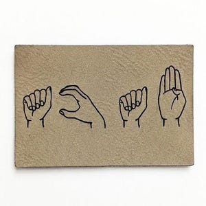 Peut inclure: Un patch rectangulaire en cuir beige clair avec des dessins au trait noirs de gestes de la main épelant un mot en langue des signes française. Les mains sont représentées dans différentes positions, avec les doigts tendus et courbés.