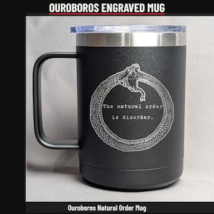 May include: A matte black insulated mug with a handle and a clear lid. The front features a laser-engraved Ouroboros snake design encircling the text: The natural order is disorder. The mug has a metallic silver rim at the top.