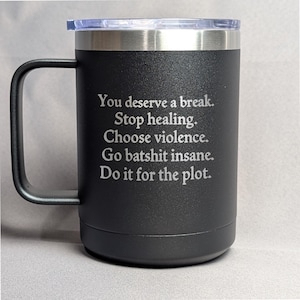 May include: Black insulated travel mug with a silver rim and handle. The mug has a clear plastic lid and features the text "You deserve a break. Stop healing. Choose violence. Go batshit insane. Do it for the plot." in white lettering.