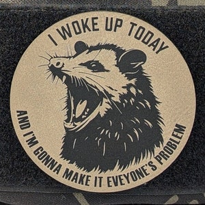 May include: A tan round patch with a black opossum illustration and the text "I woke up today and I'm gonna make it everyone's problem".
