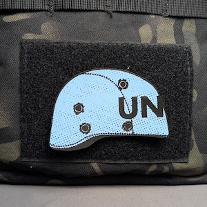 May include: A black tactical bag with a velcro patch featuring a blue helmet with the word "UN" on it.