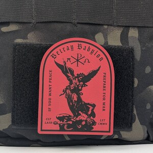May include: Red patch with black text and an image of an angel defeating a demon. The text reads "Betray Babylon", "Prepare for War", "If you want peace", "CLT LASR", and "LST CMNN".